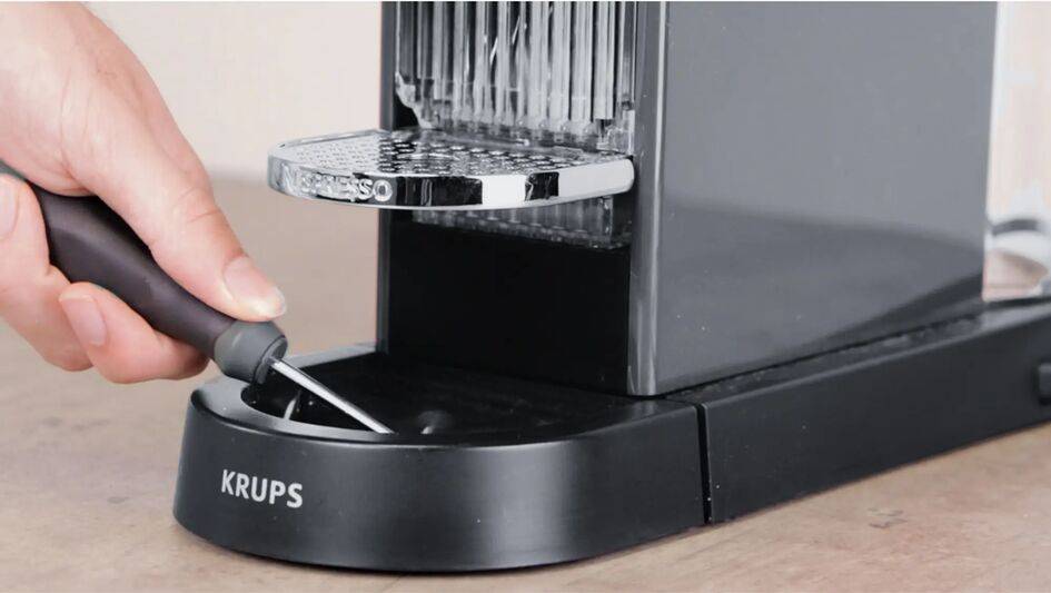 Main avec un tournevis, réparant une machine Nespresso de Krups